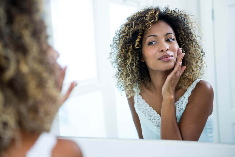 Woman looking at skin in mirror - what are pores