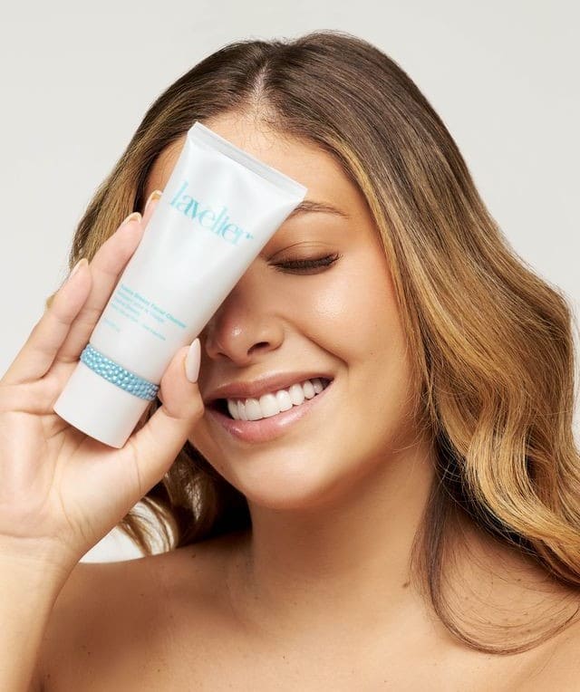 Woman holding tube of Lavelier Oceana Breezy Facial Cleanser against her face and smiling
